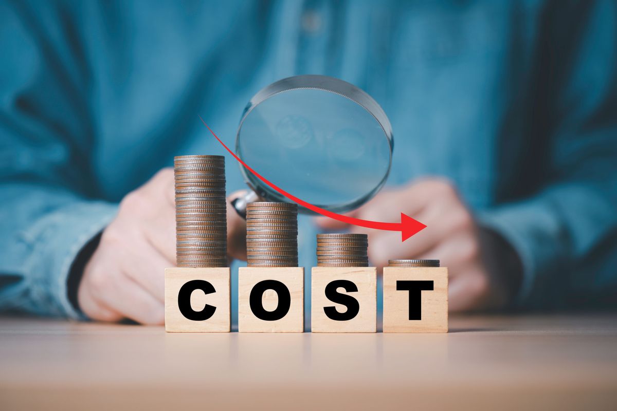 Businessman  use magnifier glass and down arrow with decreasing of coins stacking for cost reduction in factory and business cost saving  to get more profit concept.